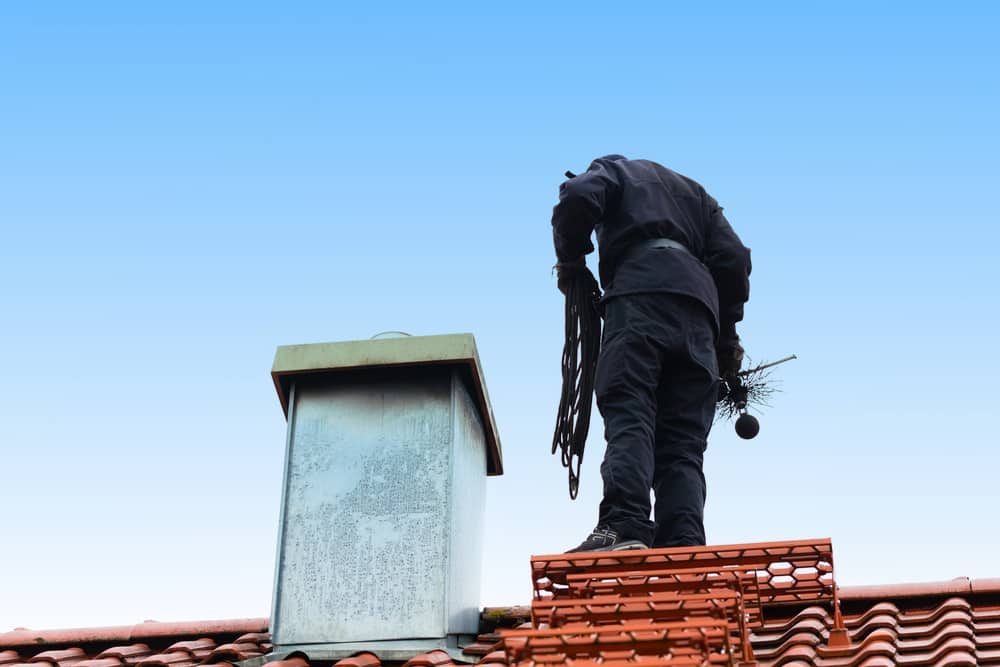 Chimney sweep standing on roof of home working Chimney sweep
